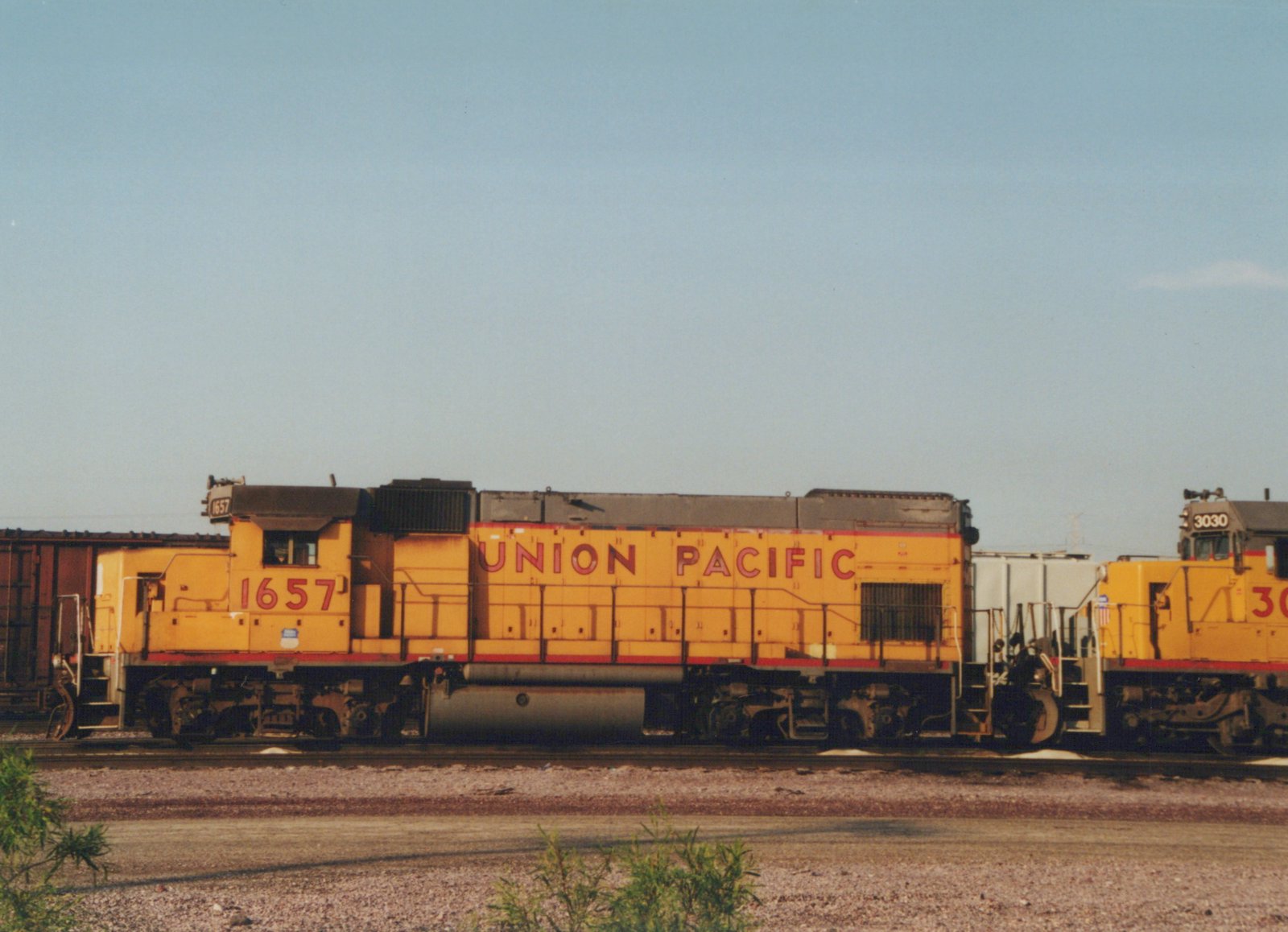 A side view of two yellow Union Pacific diesel locomotives, numbered 1657 and 3030, coupled on tracks in a gravel yard under a clear blue sky.