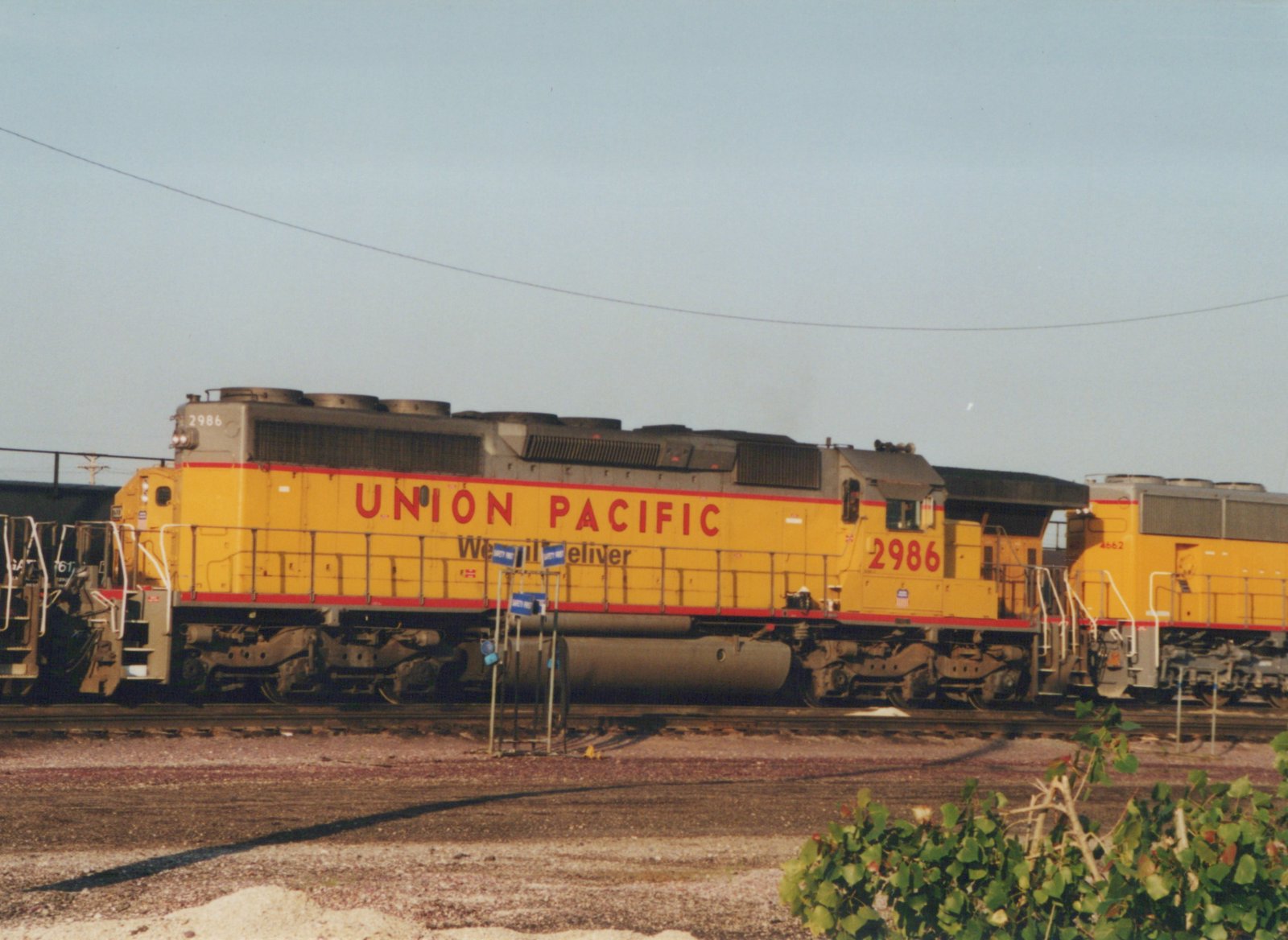 A yellow Union Pacific diesel locomotive, number 2986, is shown in side profile in a railroad yard, with another locomotive visible behind it.