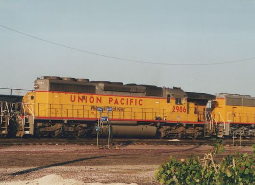 A yellow Union Pacific diesel locomotive, number 2986, is shown in side profile in a railroad yard, with another locomotive visible behind it.