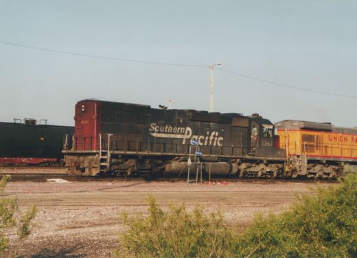 A black Southern Pacific locomotive numbered 9343 sits on tracks with a yellow Union Pacific locomotive behind it in a railroad yard on a sunny day.