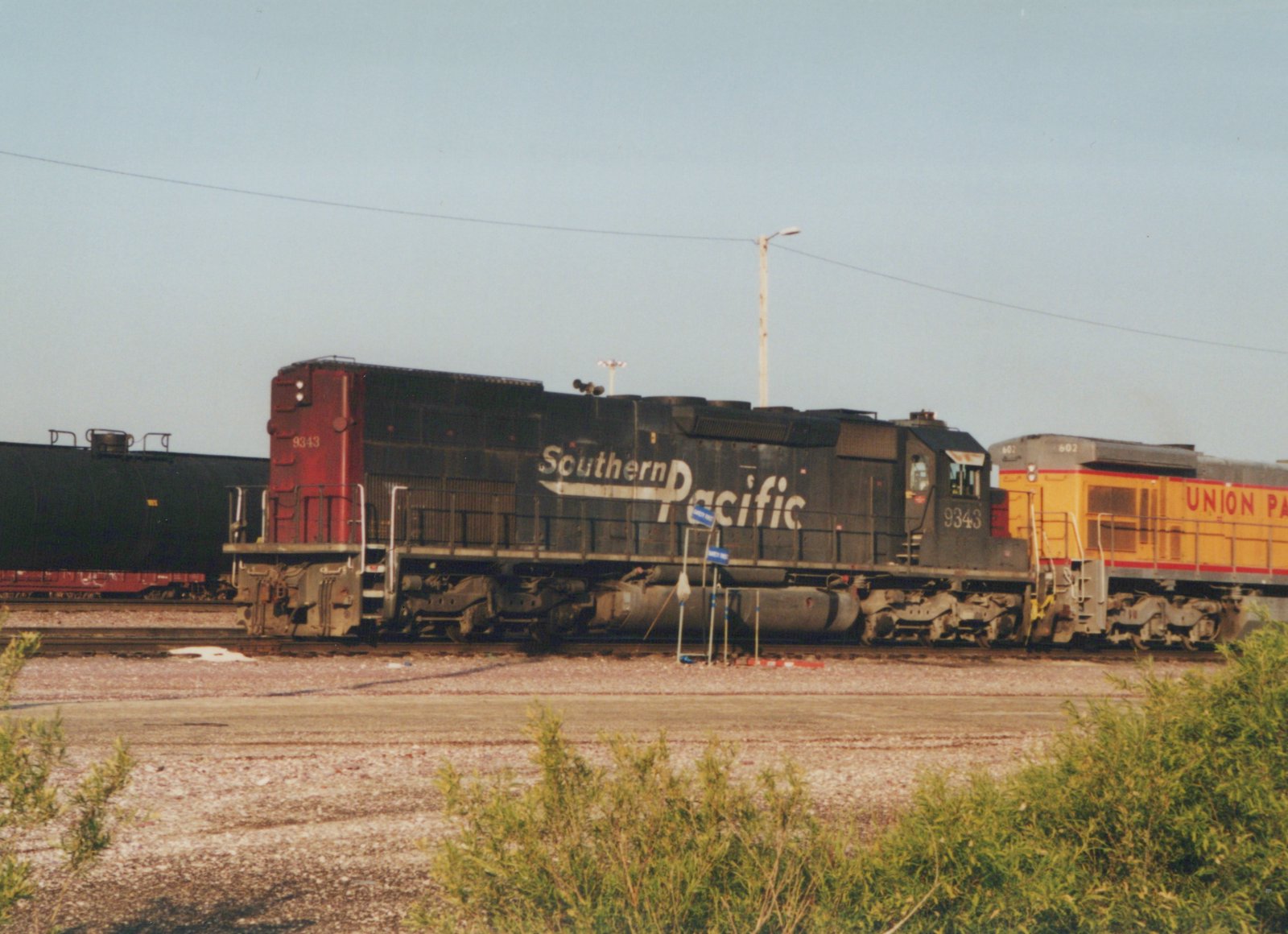 A black Southern Pacific locomotive numbered 9343 sits on tracks with a yellow Union Pacific locomotive behind it in a railroad yard on a sunny day.