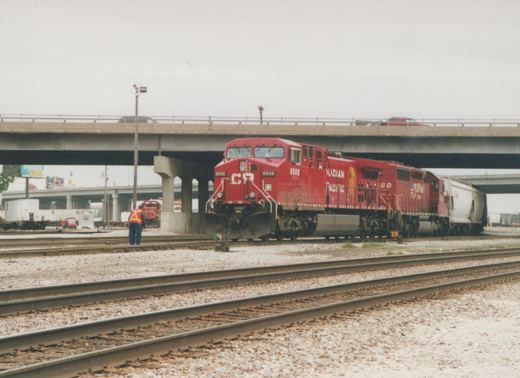 A red Canadian Pacific diesel locomotive numbered 8508 is on a set of tracks with a freight car behind it, a worker nearby, and a concrete overpass overhead.