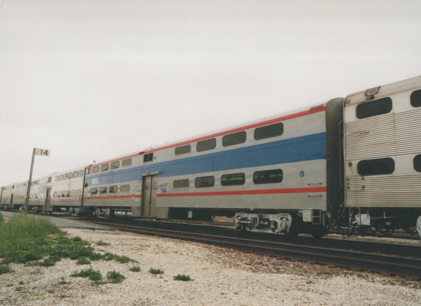 A side view of an Amtrak Superliner passenger car, number 3740, in a rail yard under an overcast sky.