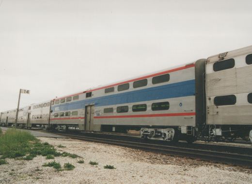 A side view of an Amtrak Superliner passenger car, number 3740, in a rail yard under an overcast sky.