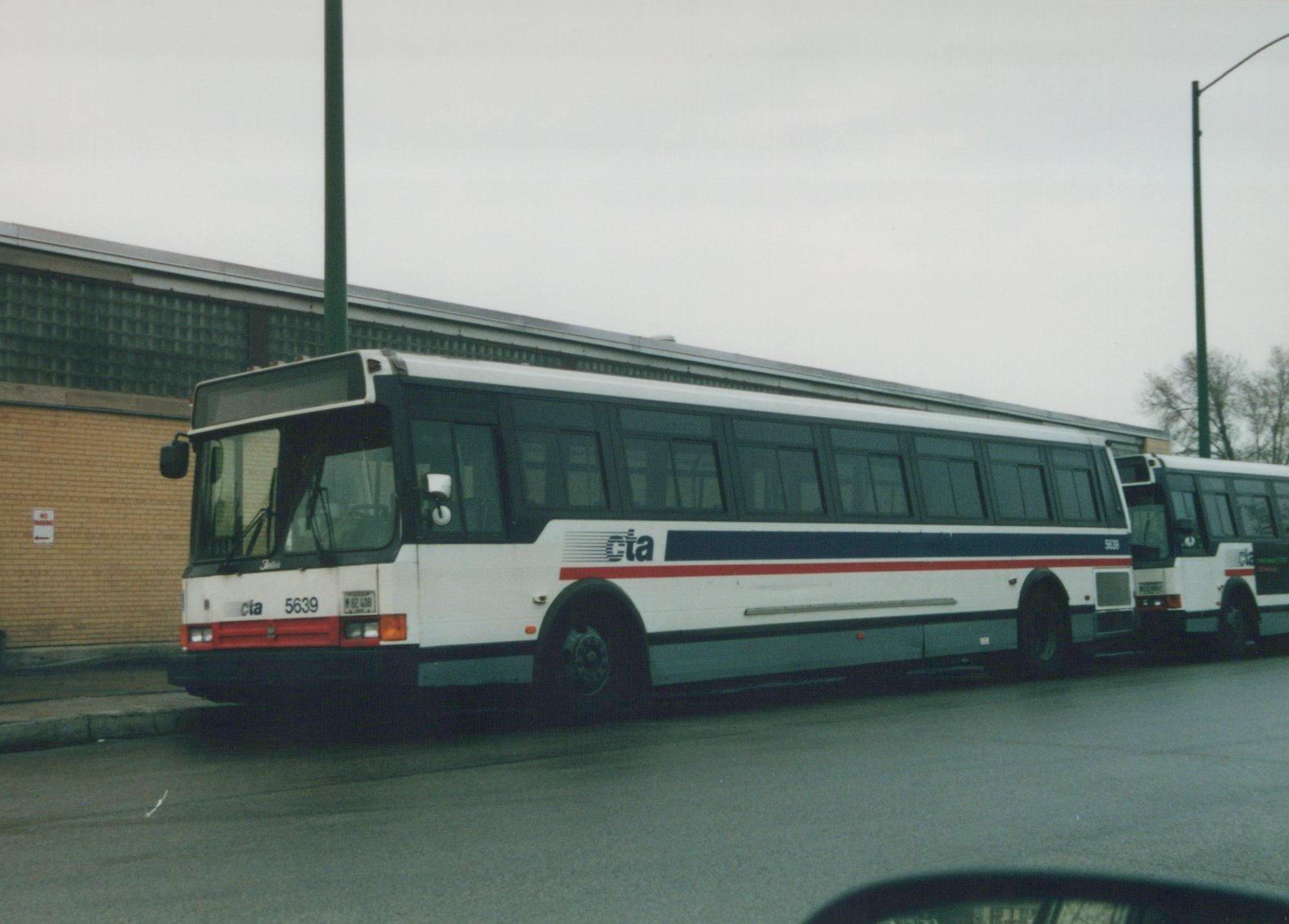 A white Chicago Transit Authority bus, number 5639, with blue and red stripes, parked on a street next to a brick building.