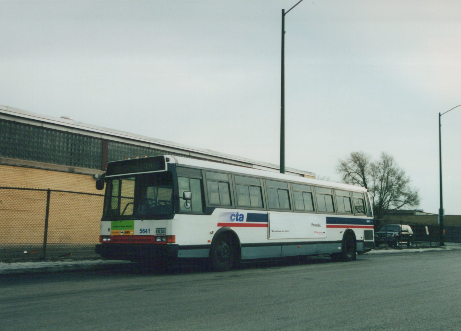 A white Chicago Transit Authority motor bus with blue and red stripes, fleet number 5641, is parked on a street with bare trees in the background under an overcast sky.
