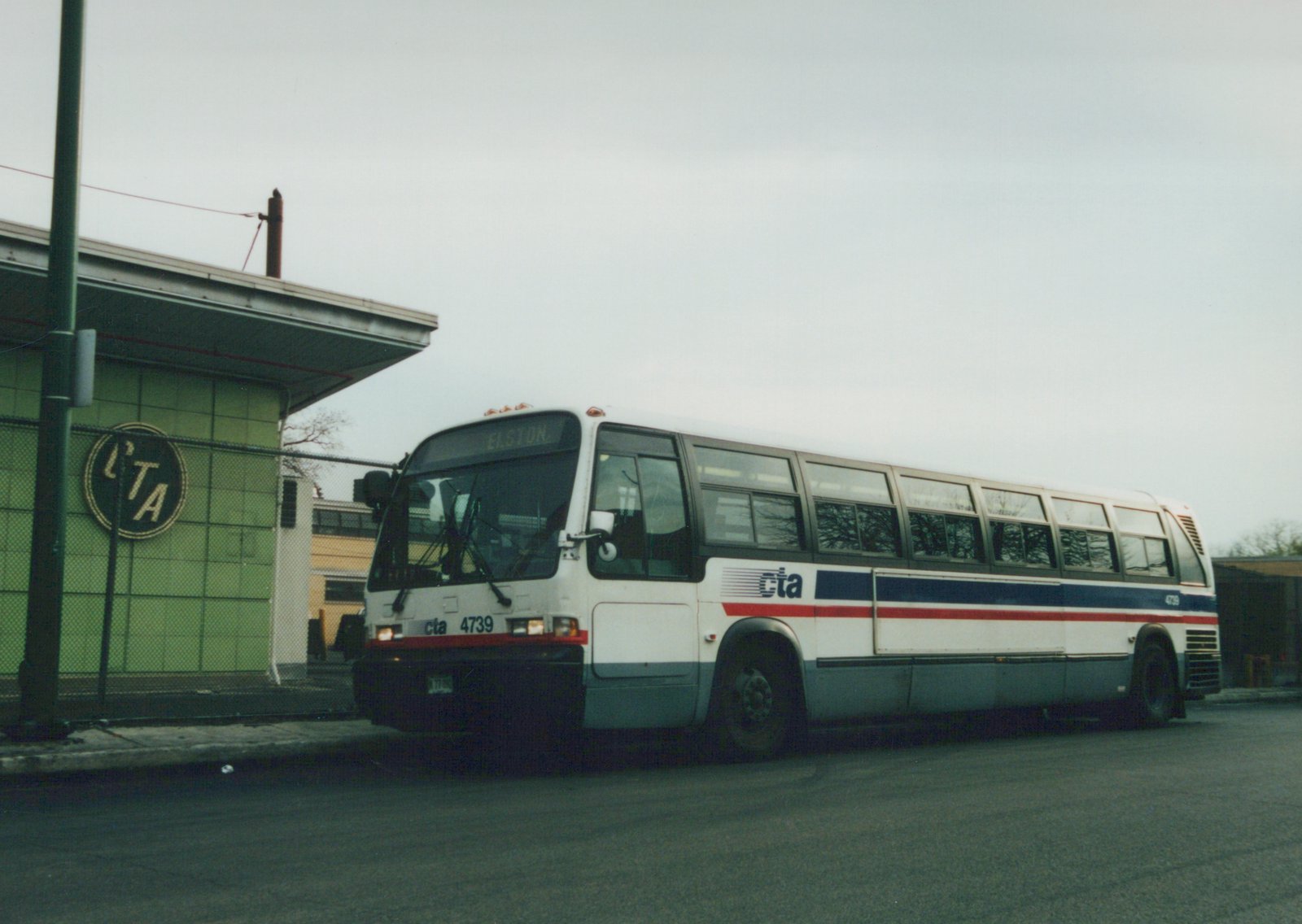 A white and blue Chicago Transit Authority bus, number 4739, is parked on a street with a green building featuring an 'LTA' sign in the background, under an overcast sky.