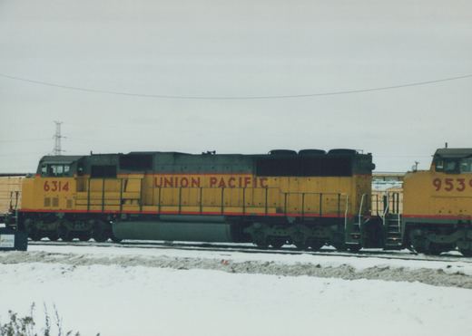 Side view of two yellow and gray Union Pacific diesel locomotives, numbered 6314 and 9539, on a snow-covered train yard under an overcast sky.