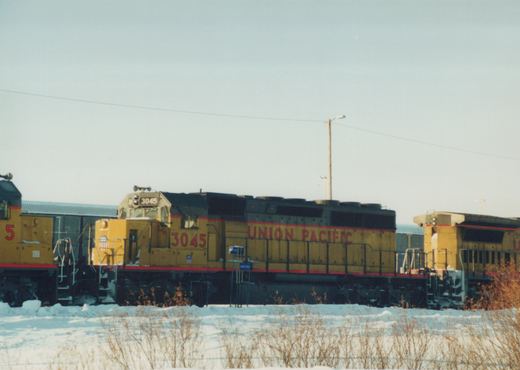 Union Pacific GP38-2 locomotive 3045 in yellow, black, and red livery, side view, in a snowy yard with another locomotive nearby.