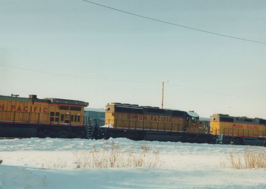 Three yellow and red Union Pacific locomotives, numbers 3645 and 375 visible, are parked side-by-side in a snowy field under a clear sky.