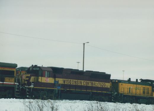 Two Wisconsin Central diesel locomotives, numbers 7520 and 1307, are coupled together in a snowy yard under an overcast sky.