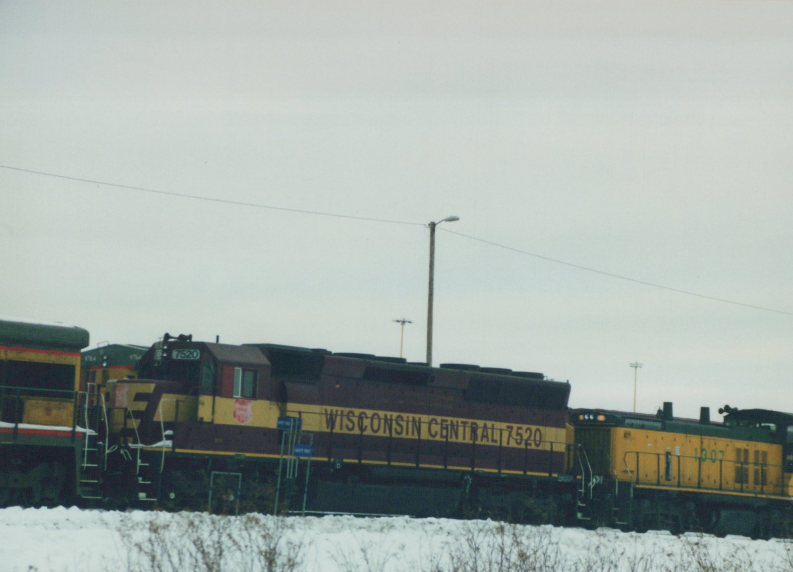 Two Wisconsin Central diesel locomotives, numbers 7520 and 1307, are coupled together in a snowy yard under an overcast sky.