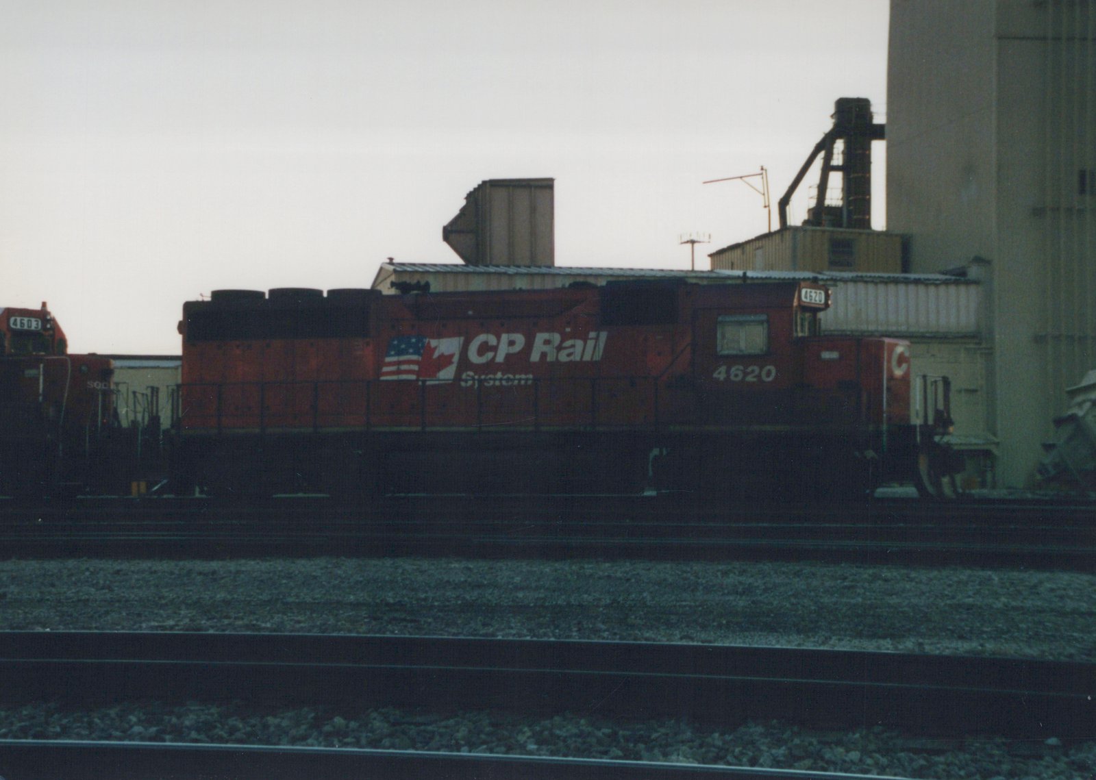 A red CP Rail System diesel locomotive with the number 4620 sits on tracks in a rail yard, with industrial buildings in the background under an overcast sky.
