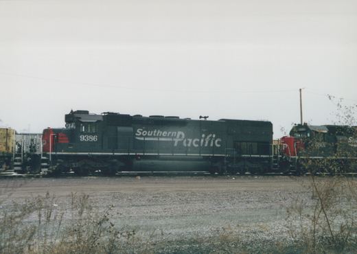 Two black Southern Pacific diesel locomotives numbered 9386 and 5801 are parked side by side in a gravel yard with dry brush in the foreground.