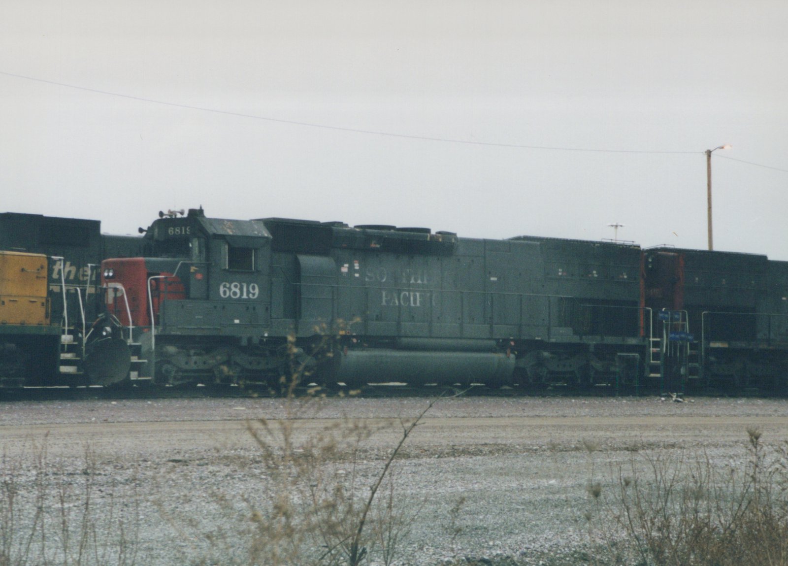 A black Southern Pacific GP9 locomotive with the number 6819 on its side, coupled to freight cars in a gravel yard under an overcast sky.