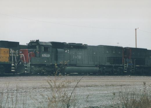 A black Southern Pacific GP9 locomotive with the number 6819 on its side, coupled to freight cars in a gravel yard under an overcast sky.