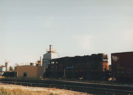 A dark green Soo Line locomotive with orange stripes, number 4512, is parked next to tracks with a blue 'Mannhiem' station sign and a CP freight car nearby.