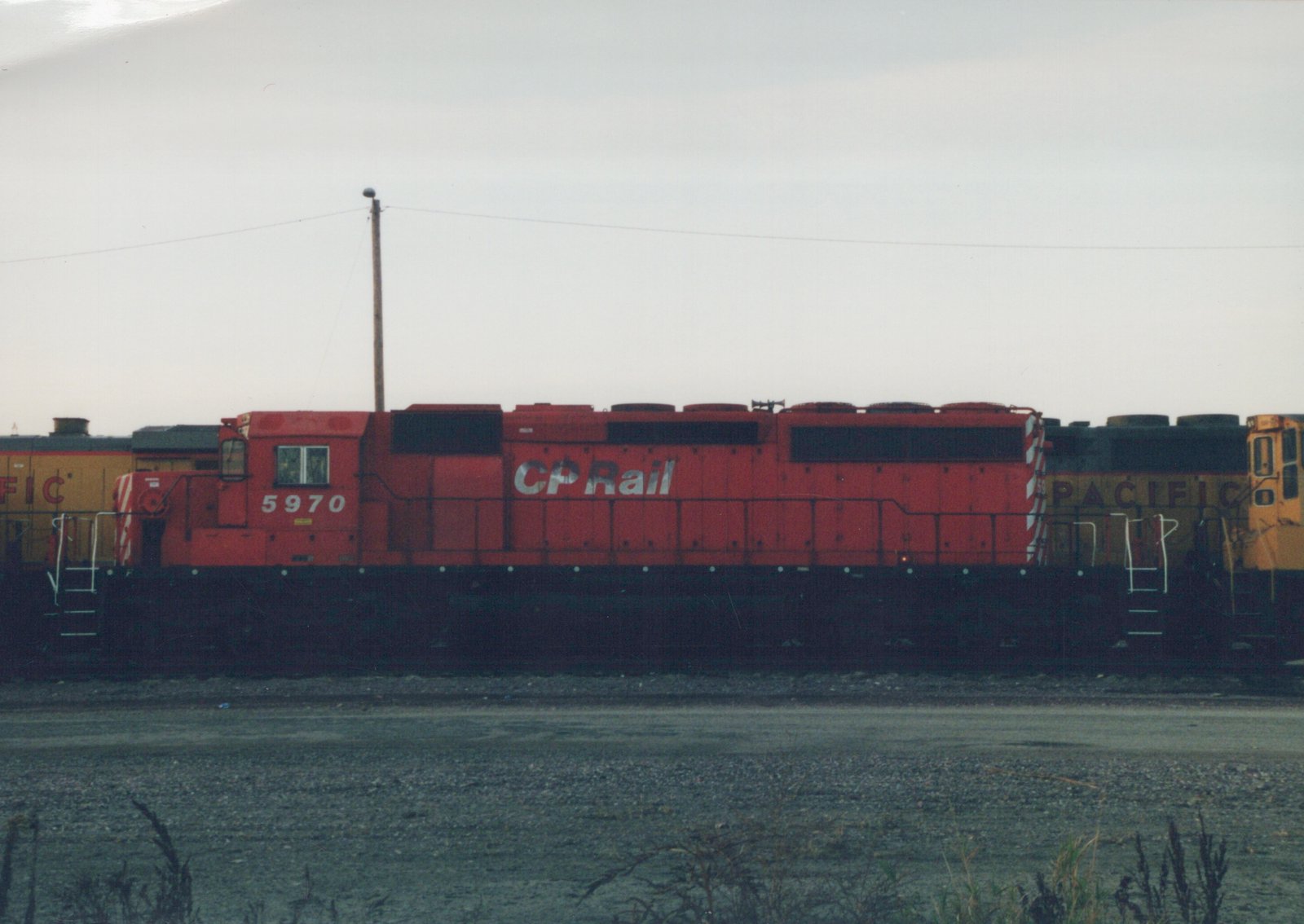 A red Canadian Pacific GP9 diesel locomotive numbered 5970 sits on tracks in a rail yard, with a yellow locomotive partially visible behind it.