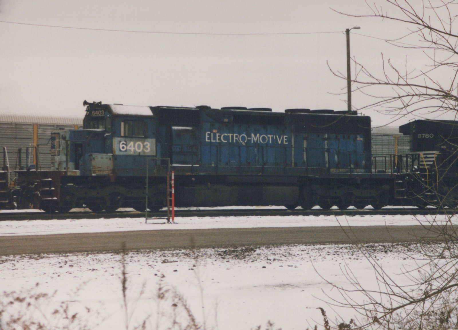 A side view of a blue EMD SD40 locomotive numbered 6403 in a snowy yard, with another locomotive, number 8780, visible behind it.