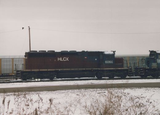 Two HLCX diesel locomotives with numbers 6066 and 6403 are parked side by side in a snowy rail yard, with a freight car marked 978749 nearby.