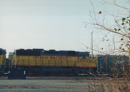 A yellow and black Union Pacific diesel locomotive with the number 5552 on its side, standing in a railroad yard with bare tree branches in the foreground.