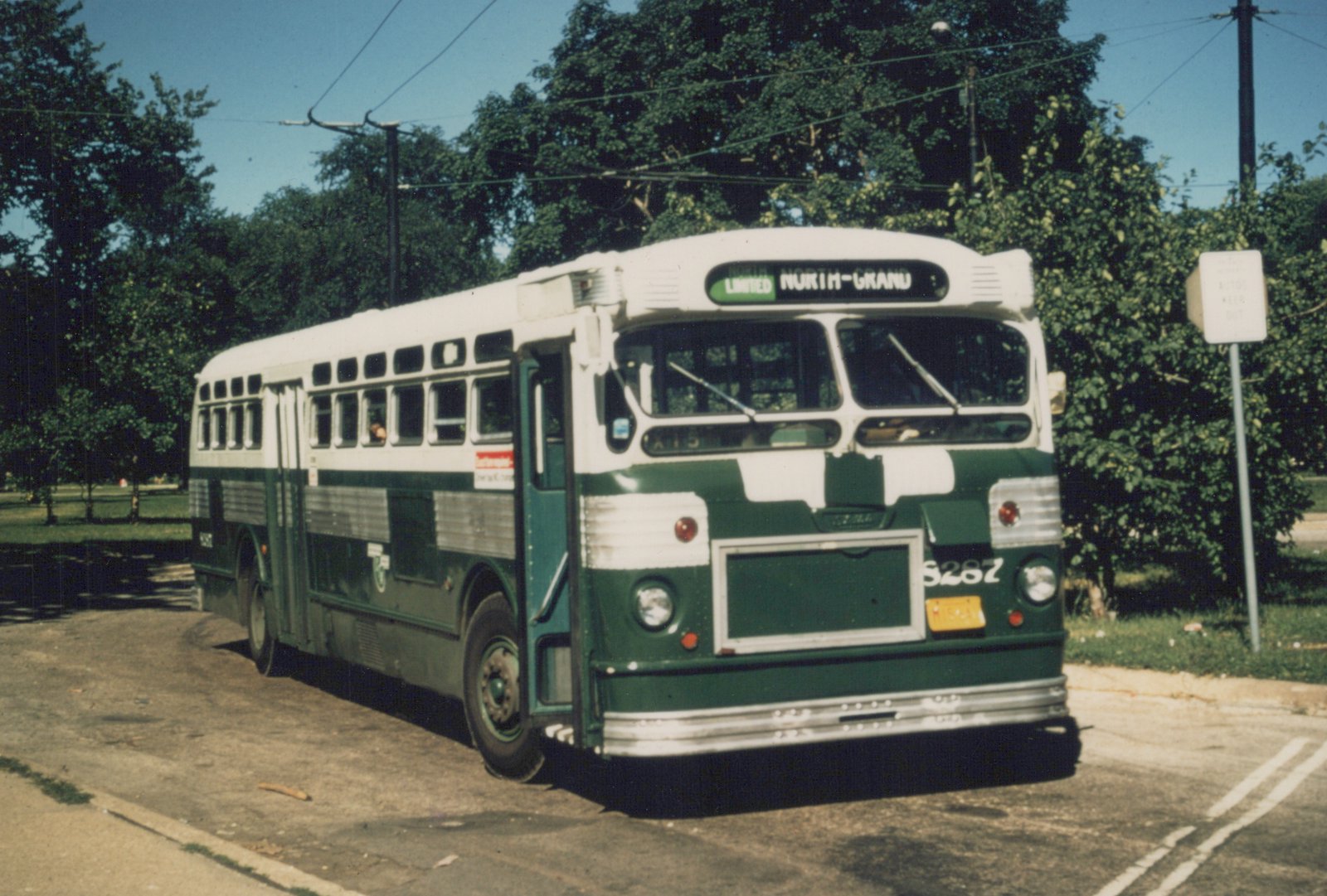 A green and white CTA bus, number 8287, is parked on a city street under a clear sky, with trees and overhead wires in the background.