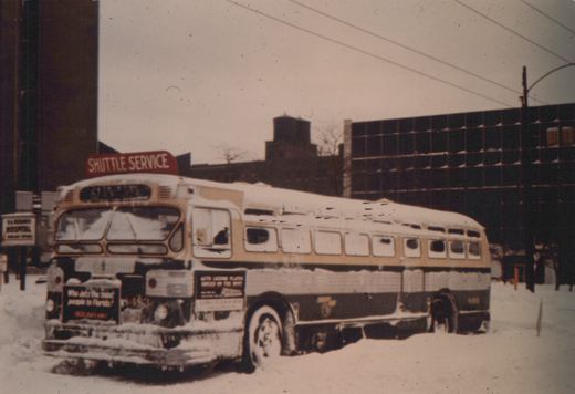 A vintage Chicago Transit Authority bus, number 483, parked in the snow with a 'Shuttle Service' sign on its roof and advertisements on its body.