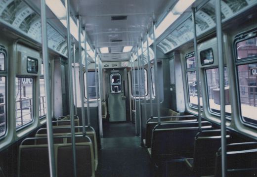 Looking down the aisle of an empty CTA 2000-series 'L' car, number 3204, at an elevated station with a passenger on the platform visible through the window.