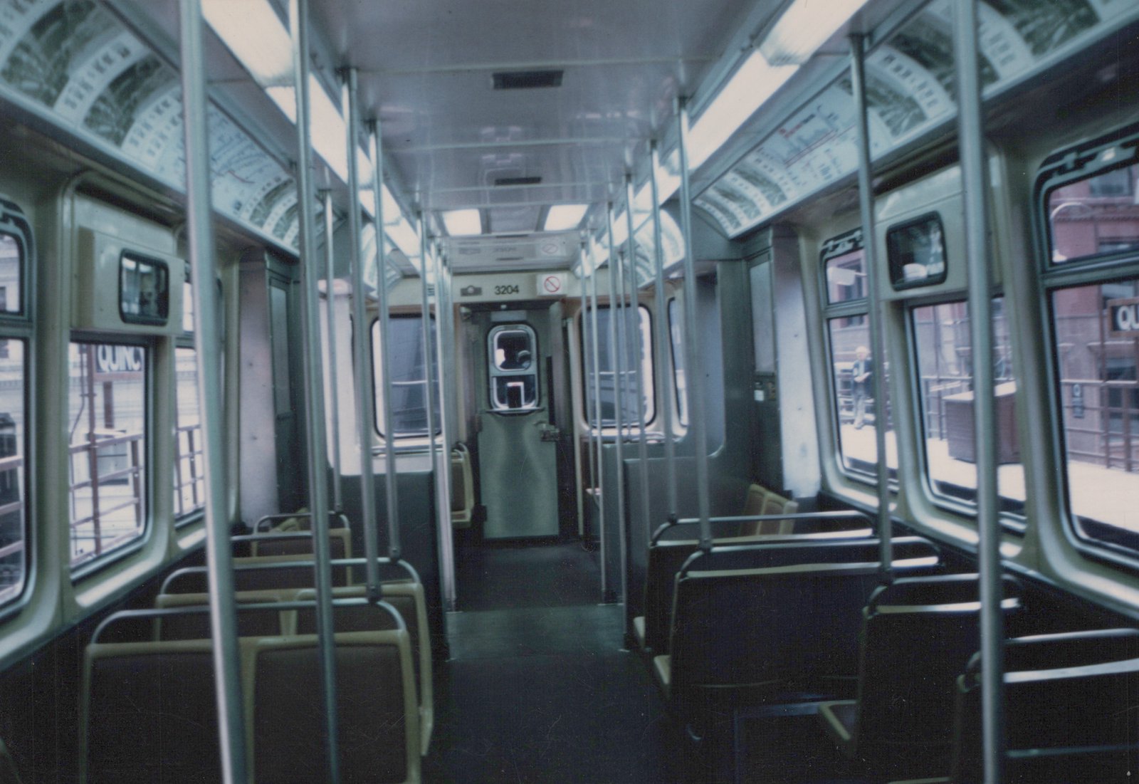 Looking down the aisle of an empty CTA 2000-series 'L' car, number 3204, at an elevated station with a passenger on the platform visible through the window.
