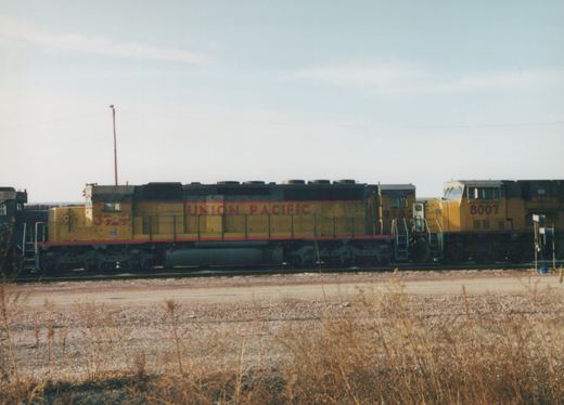 Side view of a consist of three Union Pacific diesel locomotives in a yard, displaying numbers 3929, 9182, and 8007.