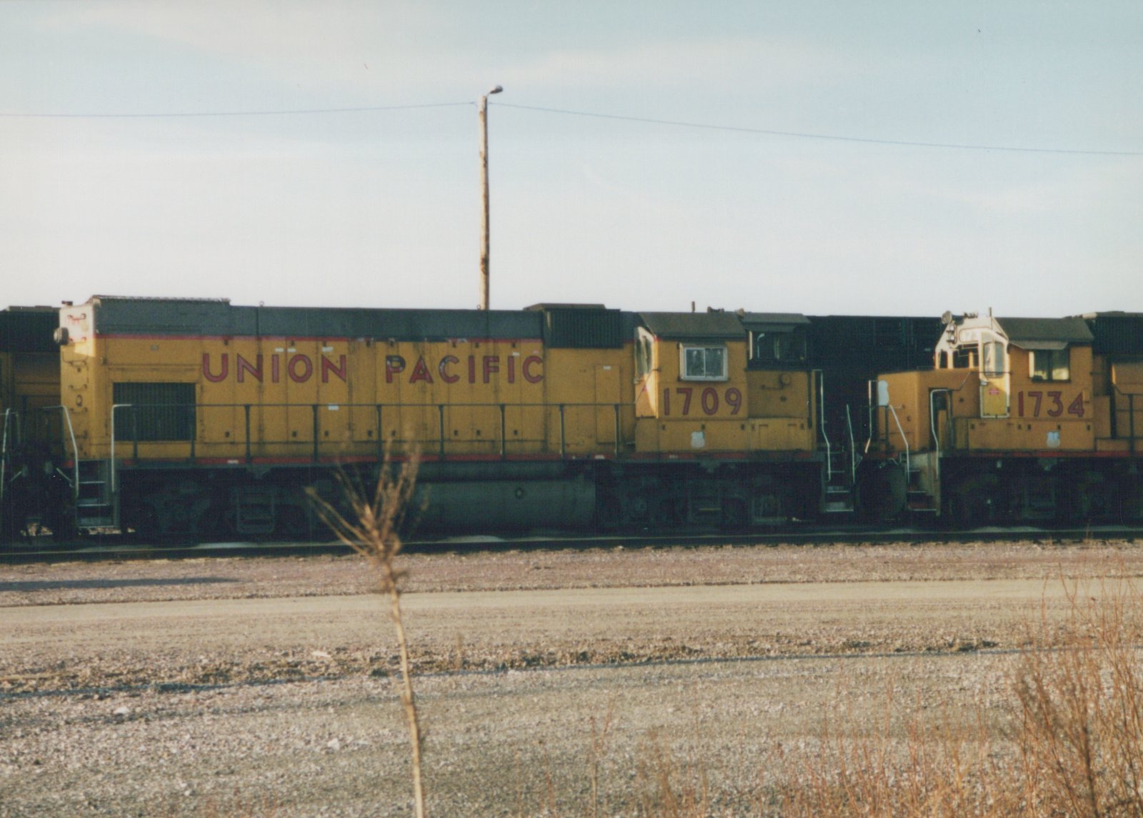 Two yellow Union Pacific diesel locomotives, numbered 1709 and 1734, are parked side-by-side in a gravel yard on a clear day.