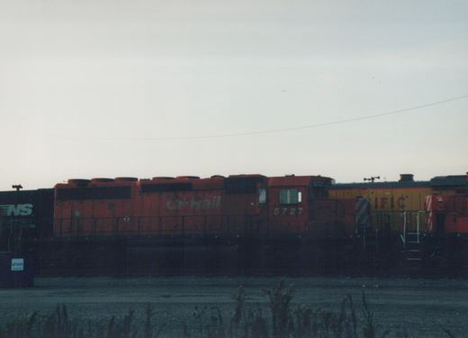 Side view of an orange Canadian Pacific locomotive numbered 5727 in a rail yard with other trains, under a gray sky at dusk.