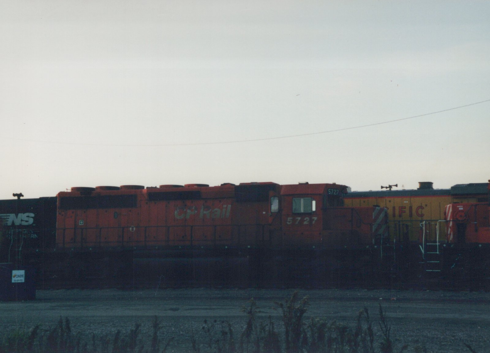Side view of an orange Canadian Pacific locomotive numbered 5727 in a rail yard with other trains, under a gray sky at dusk.