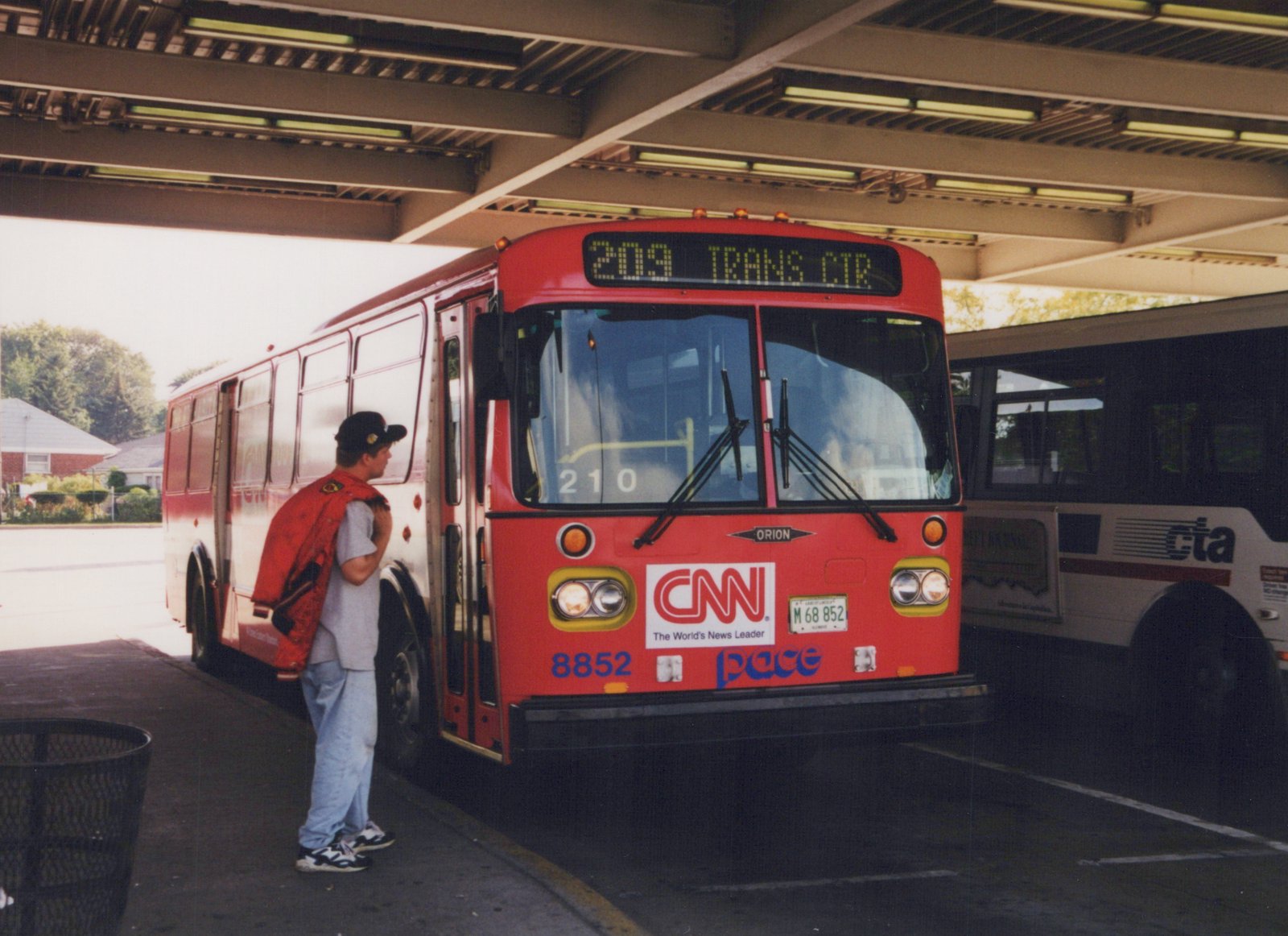 A red and white Pace bus is at a terminal with a person standing nearby; a white CTA bus is visible in the background.