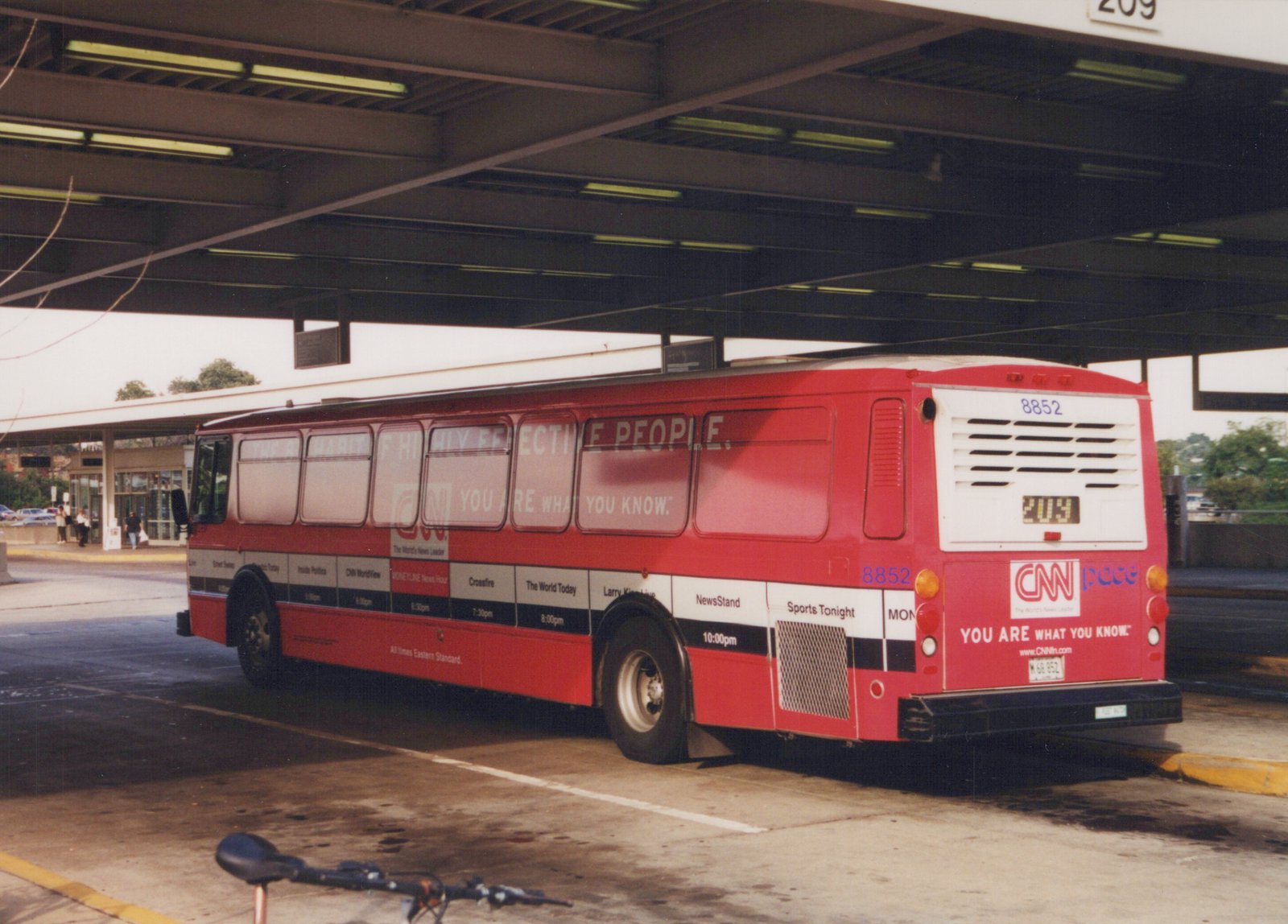 A red Pace bus with the number 8852 and a CNN ad is parked under a covered terminal structure, viewed from the rear three-quarters.