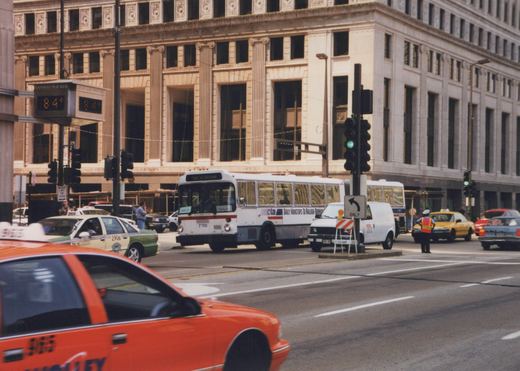 A white Chicago Transit Authority bus, number 7110, not in service, on a summer city street with taxis and a traffic cop directing traffic.