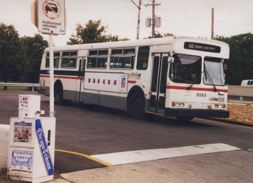 A white Chicago Transit Authority bus with red and blue stripes, number 9868, is parked on a street; a sign reads 'Authorized vehicles only cta' and a newspaper box for the Chicago Tribune is nearby.