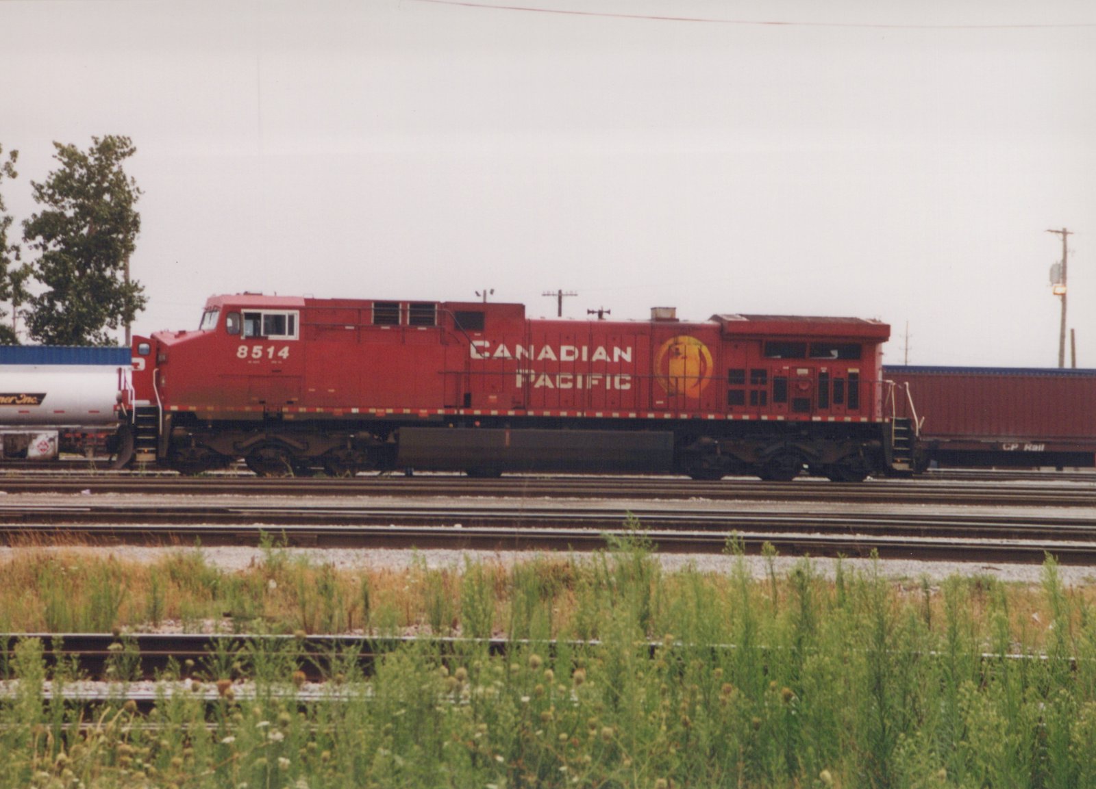 A red Canadian Pacific diesel locomotive numbered 8514 is shown on a railroad track with freight cars, under an overcast sky, with grass in the foreground.