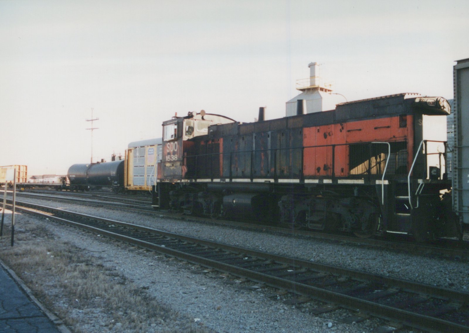 Soo Line EMD SD9 locomotive number 1538, painted in red and black, is on a set of tracks in a rail yard under an overcast sky with freight cars behind it.