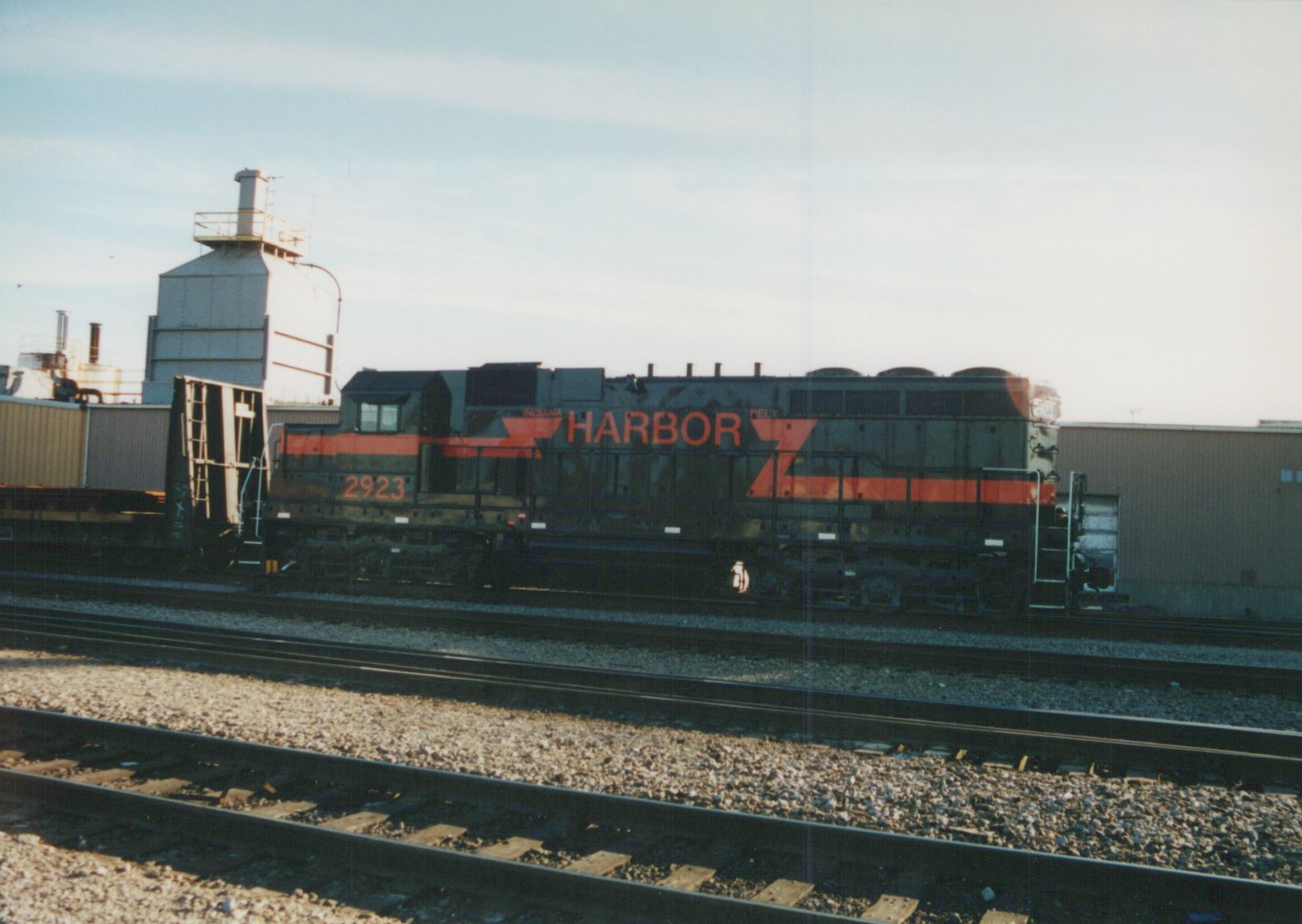 Side view of a black and orange diesel locomotive, number 2923, with 'INDIANA HARBOR BELT' lettering, sitting on a set of tracks in a rail yard.