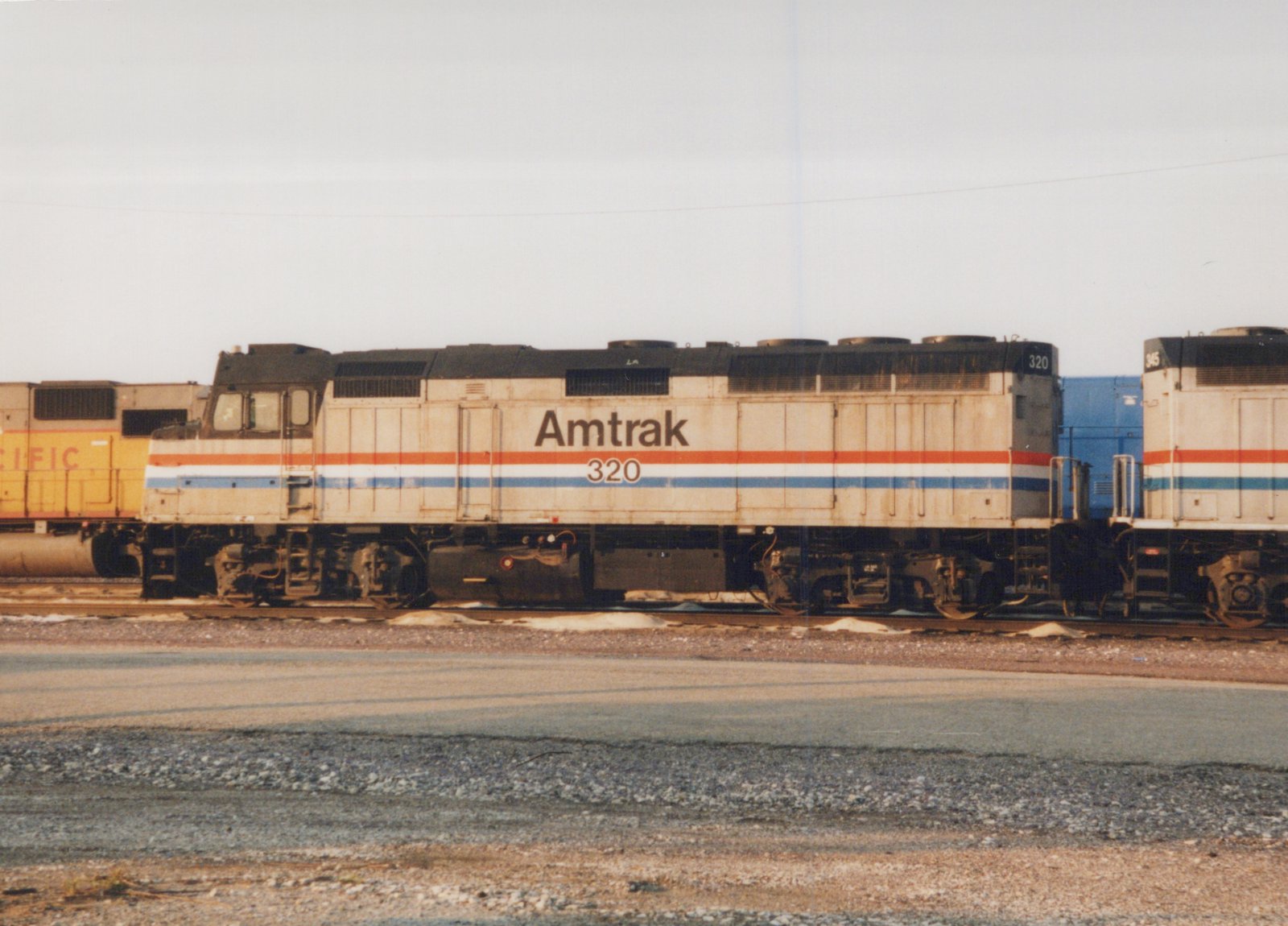 A side view of an Amtrak diesel locomotive numbered 320 in a rail yard, with other locomotives visible behind it.