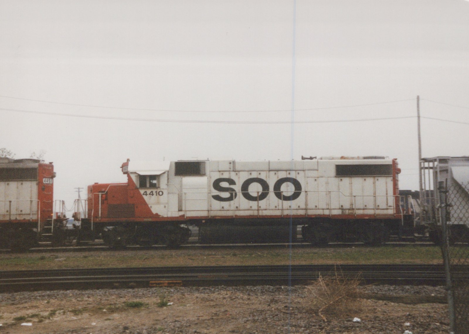 A side view of a white and orange Soo Line diesel locomotive, number 4410, parked in a rail yard next to a freight car.