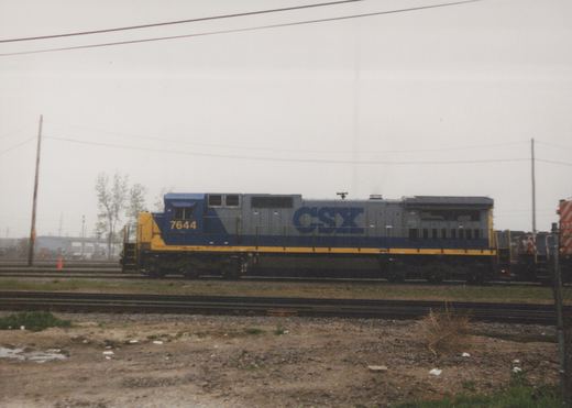 A blue and yellow CSX diesel locomotive, number 7644, is parked on railroad tracks in a gravel yard.
