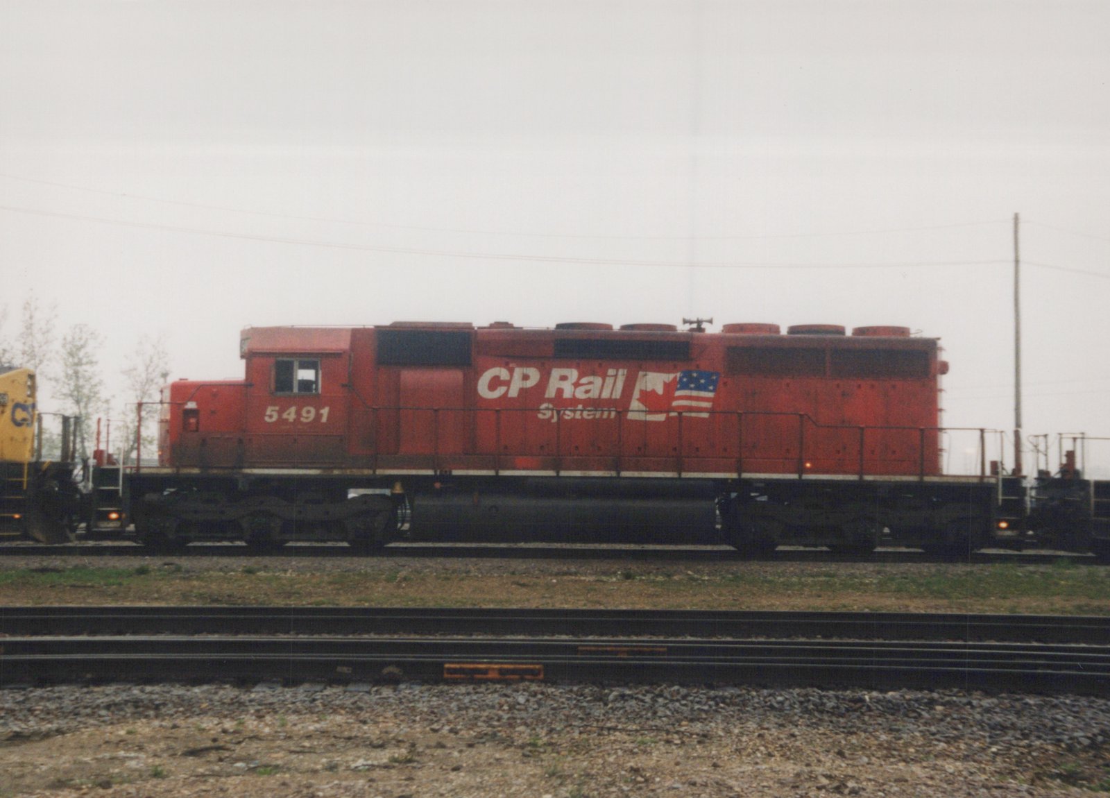 A side view of a red CP Rail System diesel locomotive, number 5491, parked on multiple tracks in a rail yard under a gray sky.