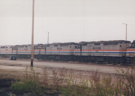 A row of Amtrak locomotives, numbered 326, 401, 314, and 325, parked side by side in a gravel yard under an overcast sky.
