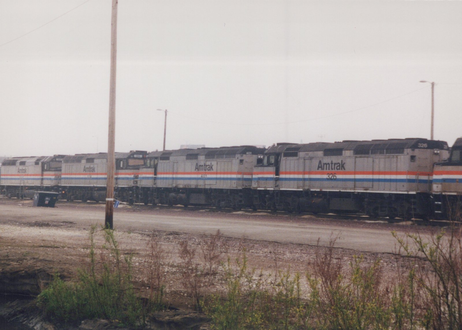 A row of Amtrak locomotives, numbered 326, 401, 314, and 325, parked side by side in a gravel yard under an overcast sky.