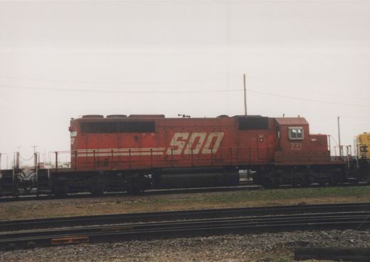 A red SOO Line diesel locomotive numbered 771 is parked on tracks in a rail yard with overcast skies.