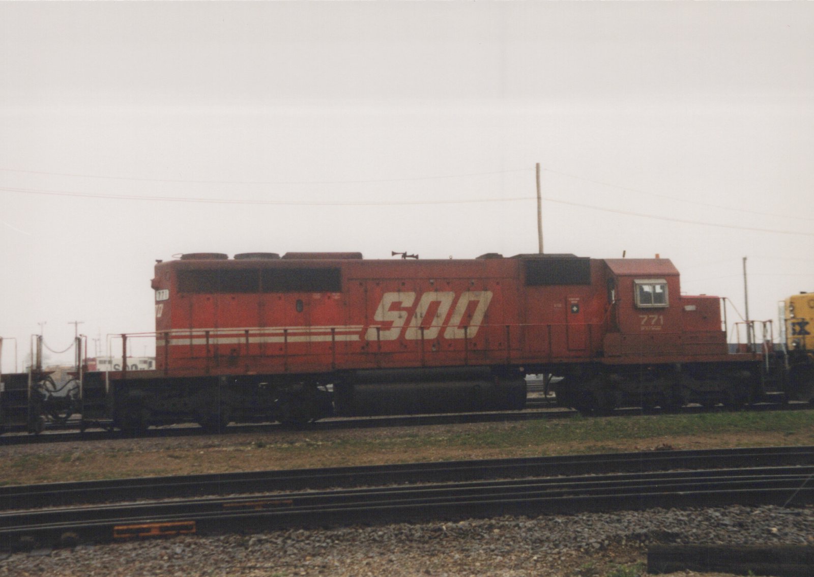 A red SOO Line diesel locomotive numbered 771 is parked on tracks in a rail yard with overcast skies.