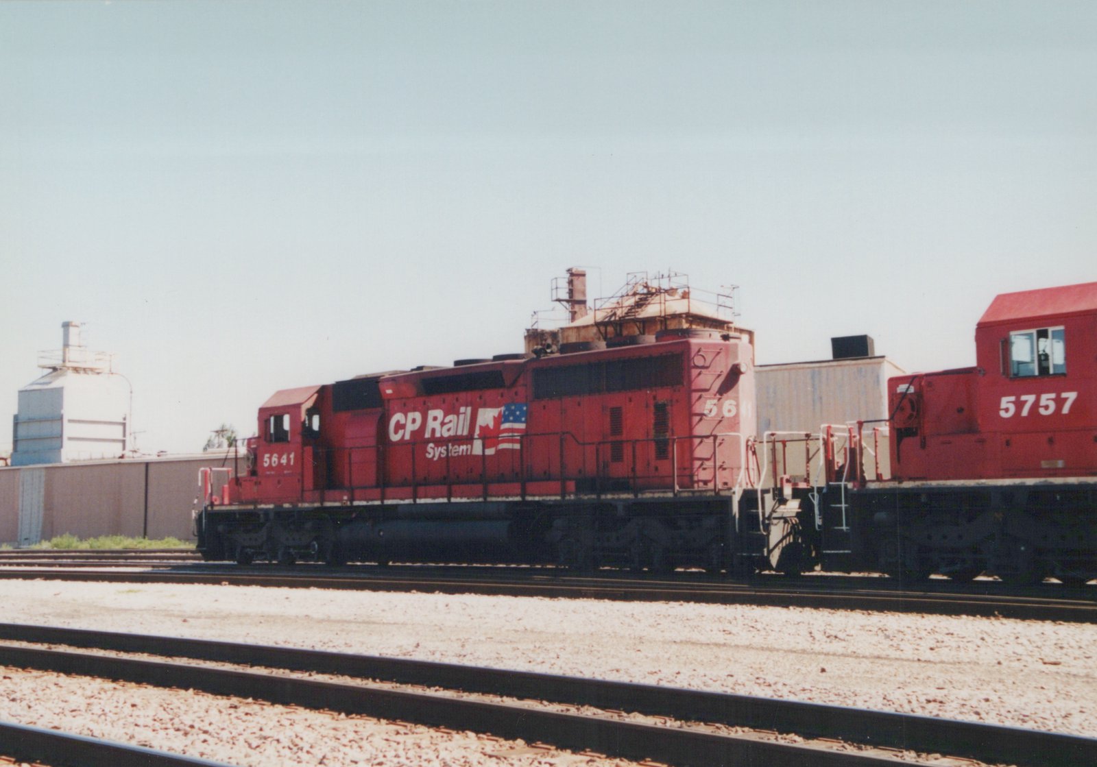 A side view of two red CP Rail System diesel locomotives, numbered 5641 and 5757, coupled on tracks in a yard with a clear sky and industrial buildings in the background.
