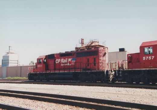 A side view of two red CP Rail System diesel locomotives, numbered 5641 and 5757, coupled on tracks in a yard with a clear sky and industrial buildings in the background.